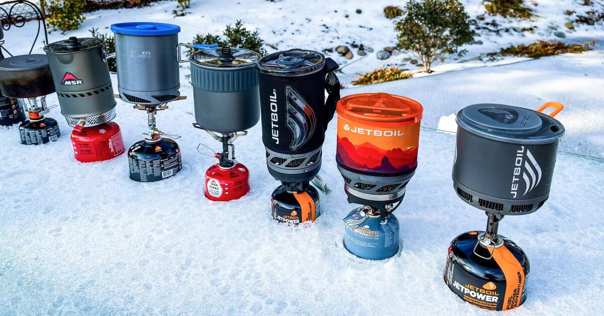Collection of ultralight backpacking stoves arranged on digital scale showing weight comparison for 2024 gear review